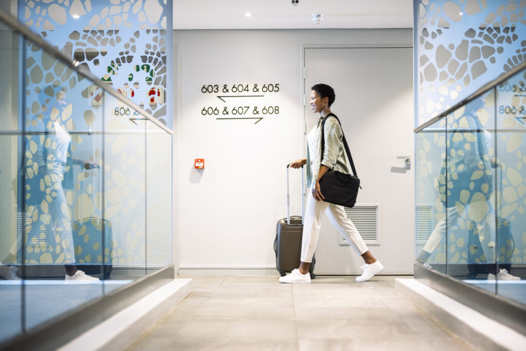 oung woman walking with wheeled luggage in hotel corridor